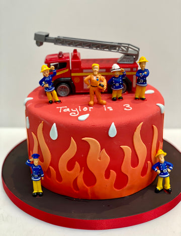 Firefighter-themed birthday cake with toy figures and fire truck on a white background