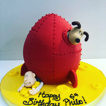 Cake carved to look like wallace and gromit's rocket with the characters peeking out of the windows delivered in london